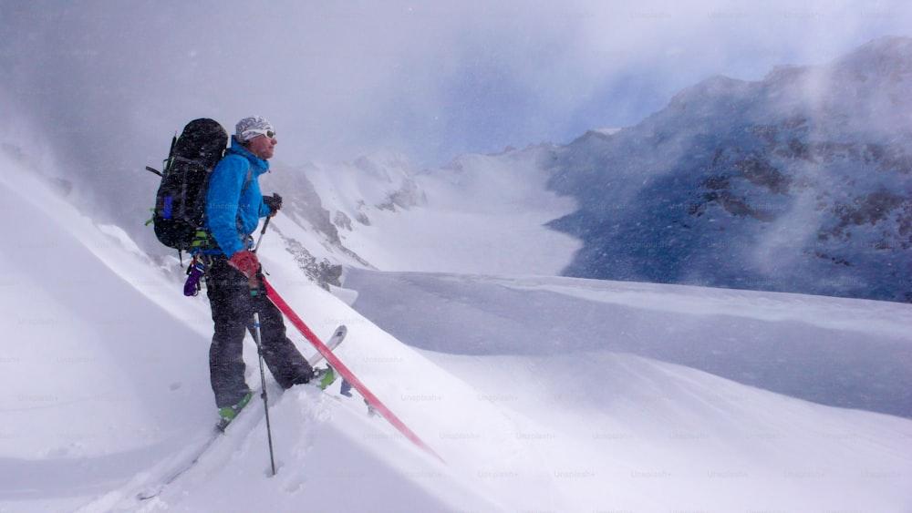 skieur de randonnée masculin en route vers un haut sommet alpin et jouant et faisant des bêtises pendant de légères chutes de neige par une belle journée d’hiver dans les Alpes suisses