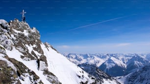 male backcountry skier at the summit cross of a high alpine peak on a beautiful winter day in the Swiss Alps