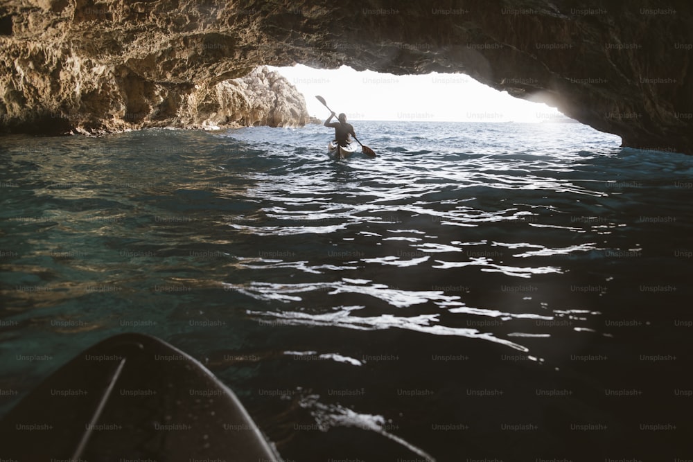 Homme pagayant en kayak dans une grotte, faisant du kayak et de la spéléologie en même temps.