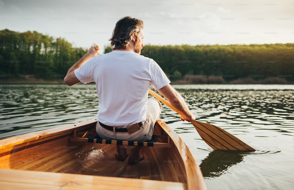 Rear view of male canoeist paddling the wooden canoe with oar.