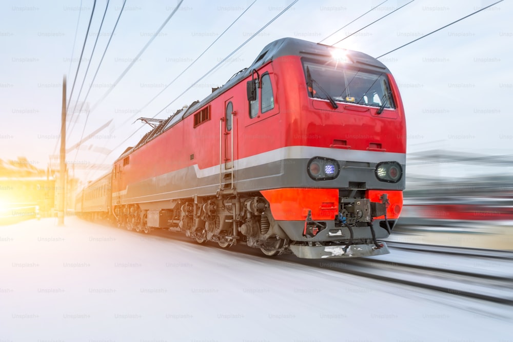 High-speed red locomotive passenger train rides at high speed in winter around the snowy landscape