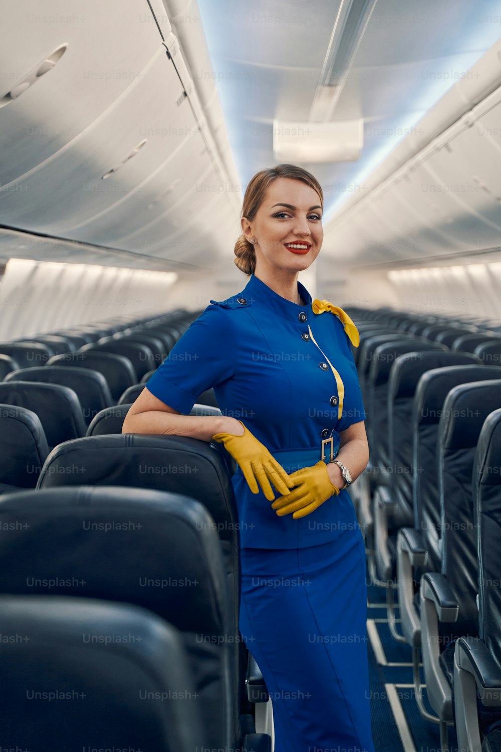 Front view of a smiling contented elegant lovely air hostess in leather gloves posing for the camera aboard the plane