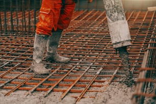 Baustellenarbeiter in Stiefeln und orangefarbenem Schutzanzug beim Betongießen.