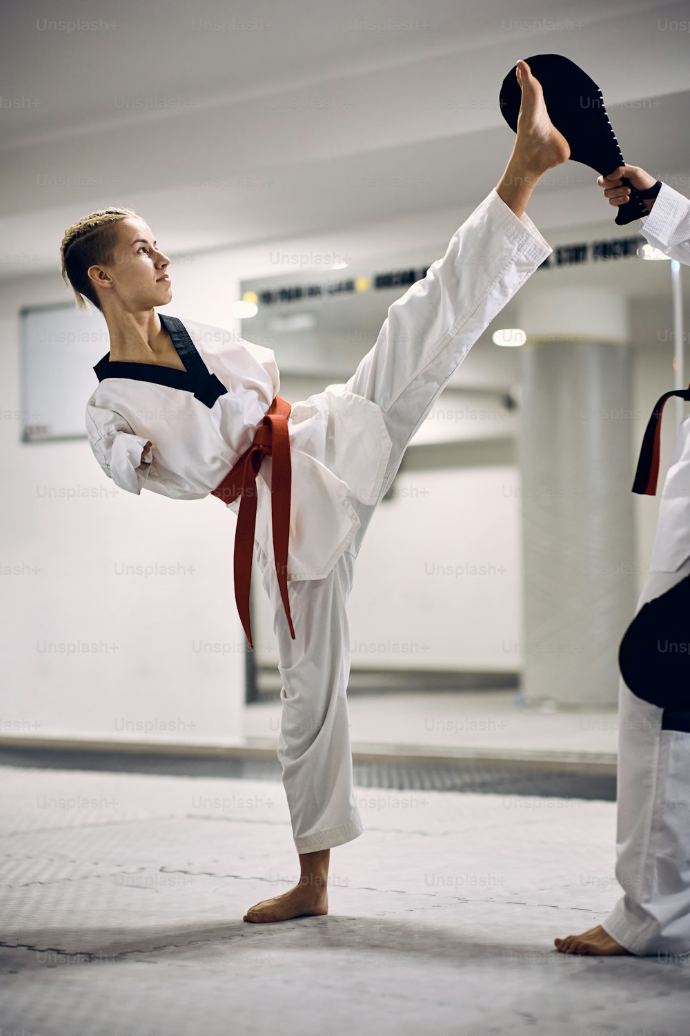 Entschlossene Taekwondo-Kämpferin mit Behinderung, die mit ihrem Trainer im Fitnessstudio High Kick übt.