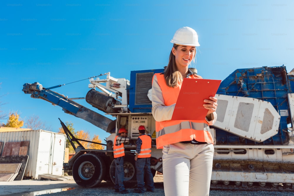 Civil Engineer woman standing with clipboard in front of stone crusher