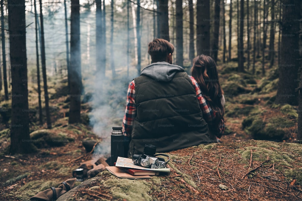 Rear view of young couple warming up by the campfire while sitting in the forest