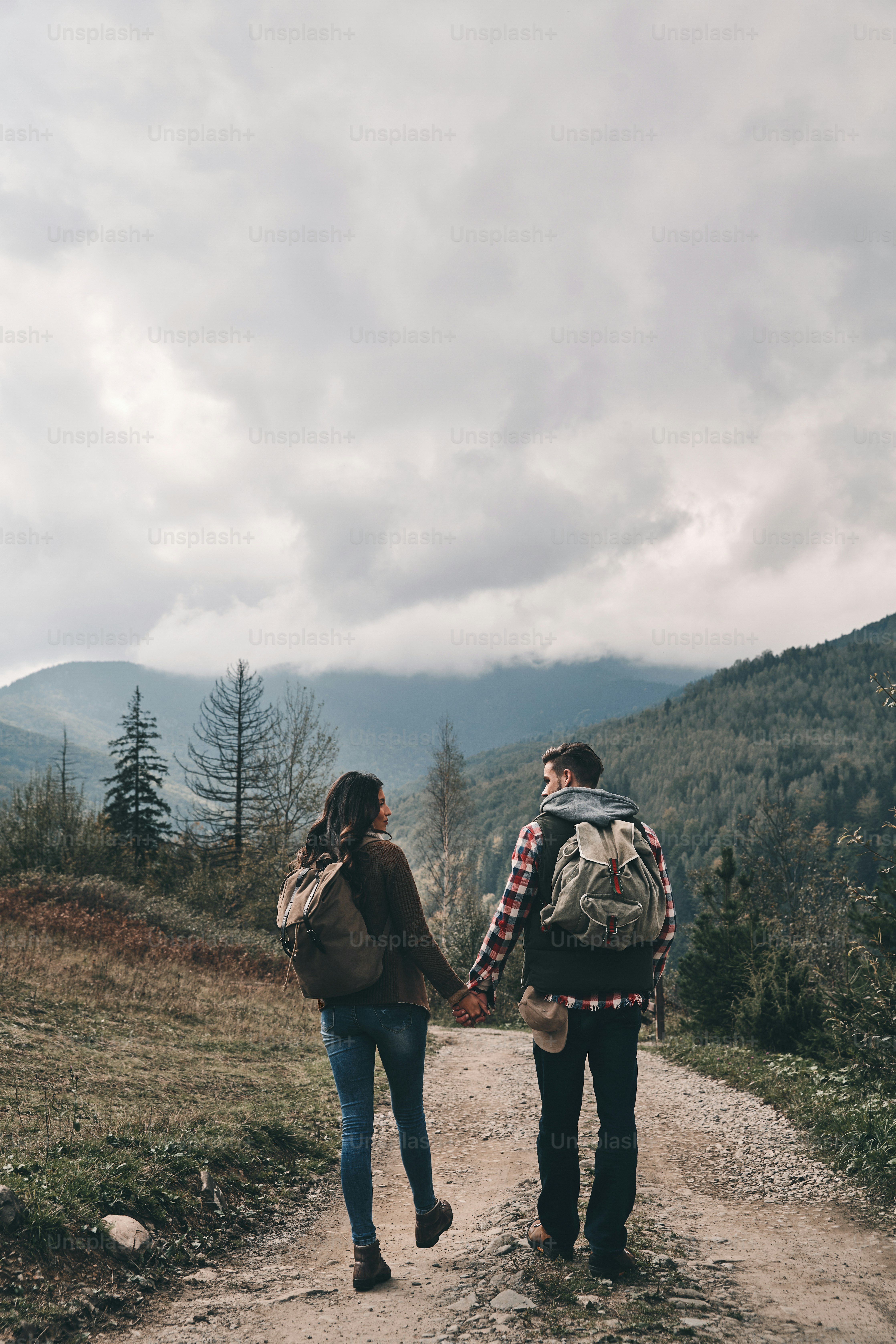 Full length rear view of young couple holding hands while hiking in ...
