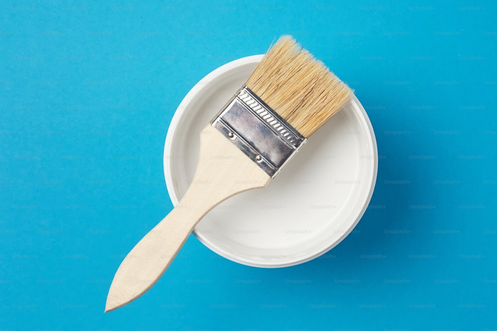 Pincel y lata de pintura con color blanco sobre fondo azul, primer plano
