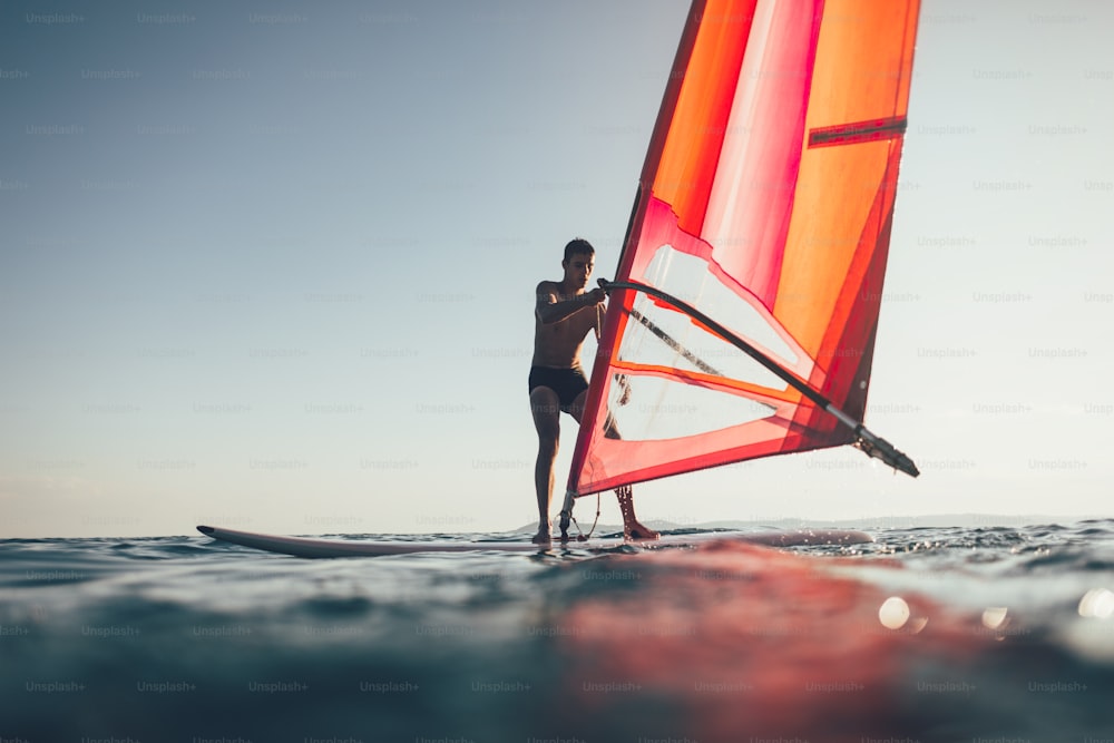 Vue en contre-plongée de la silhouette d’un surfeur en équilibre sur une planche à voile.