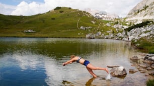 Una atractiva rubia veinteañera que se sumerge en un lago de montaña