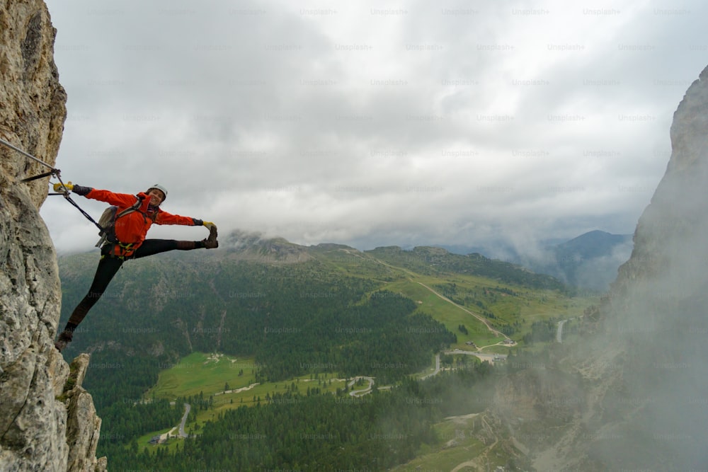 attractive young female mountain climber on a Via Ferrata in the Dolomites of Italy in bad weather in a crazy stretching pose