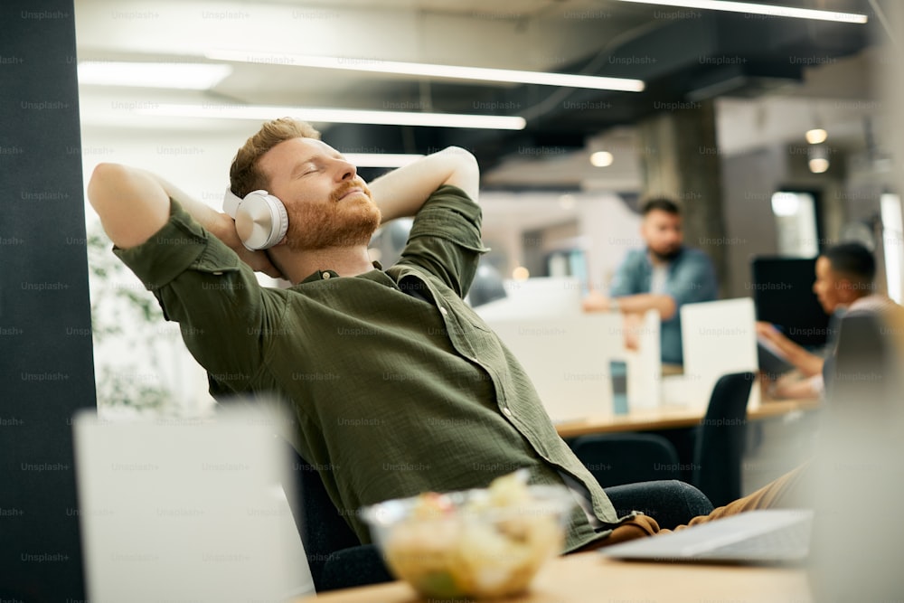 Jungunternehmer hören Musik über Kopfhörer, während er sich in einer Pause im Büro entspannt.