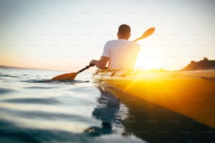 Man kayaker paddling the kayak at sunset sea.