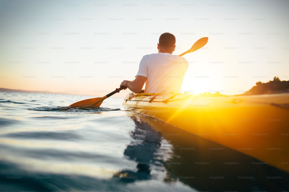 Kayakiste homme pagayant le kayak au coucher du soleil sur la mer.