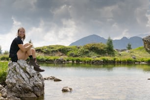 Uma morena atraente em seus vinte anos relaxando em uma pedra em um lago de montanha