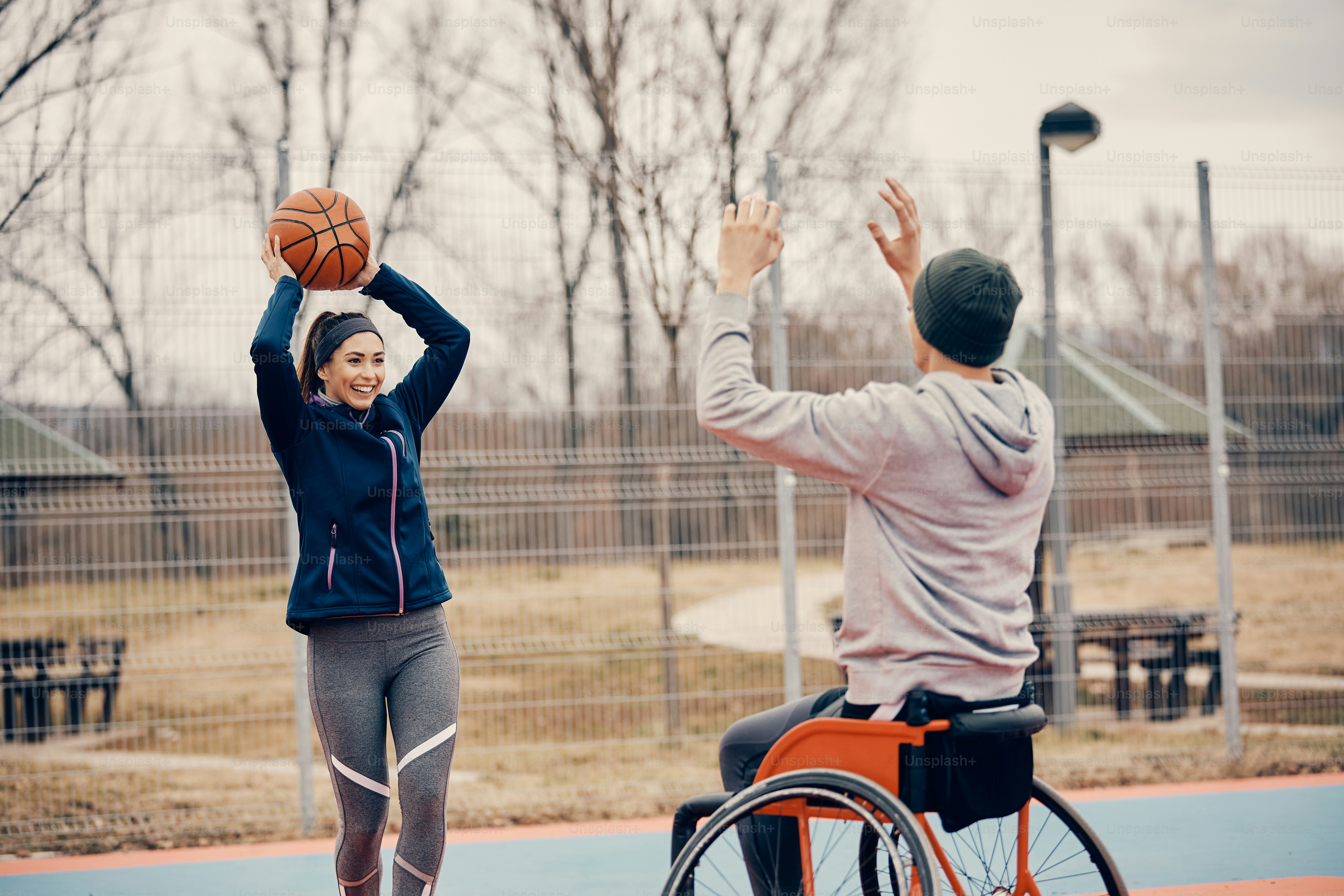Mujer atlética feliz que se divierte mientras juega baloncesto con un amigo que usa silla de ruedas.