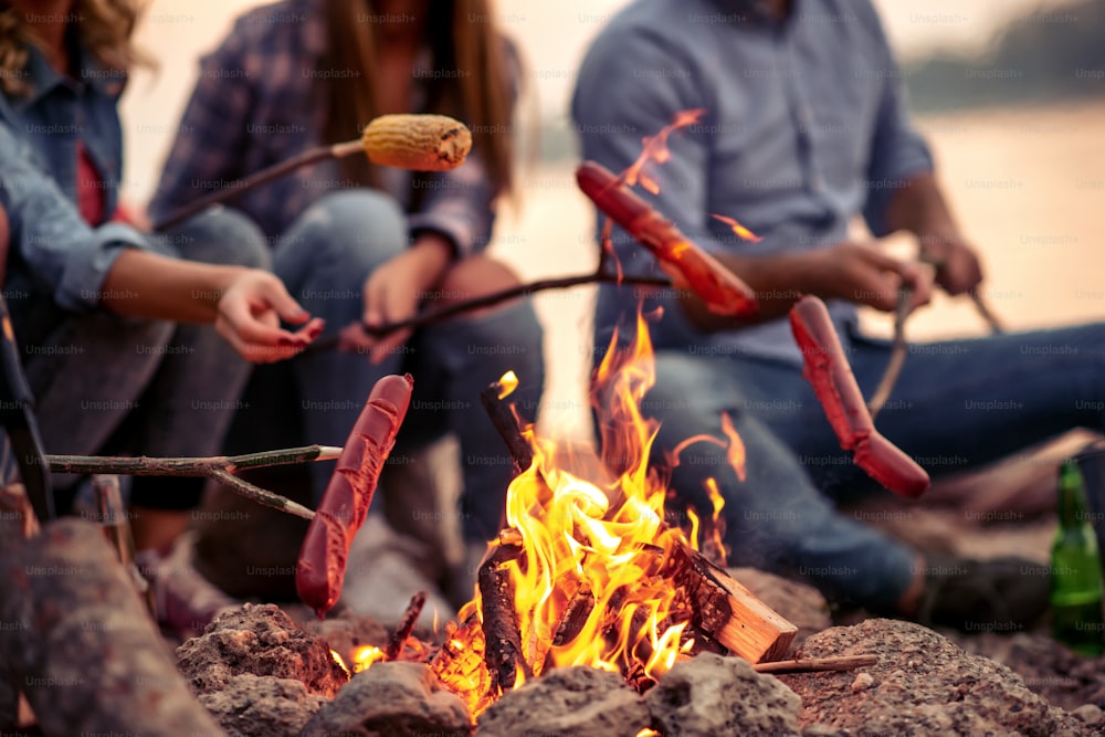 Friends grilling sausages and make hot dogs while camping.