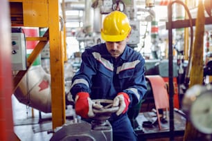 Trabalhador trabalhador da planta de energia em traje de trabalho e com capacete de proteção na válvula de parafusamento da cabeça.