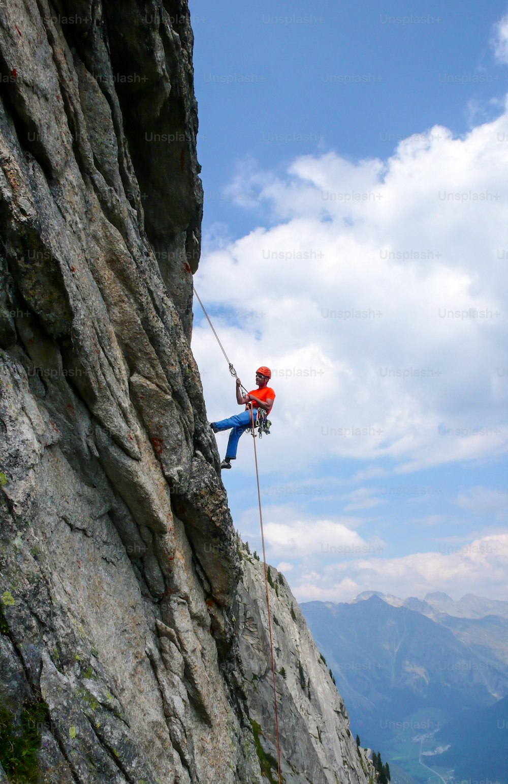A male rock climber abseiling off a steep rock climbing route in the Swiss Alps after a hard climb