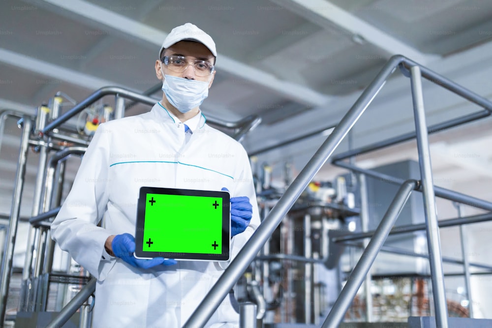 Mock-up screen for recording. The technologist in a mask, gloves and a white robe stands with a tablet with an empty screen at the factory. A man with a digital tablet in uniform in the production shop