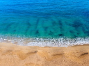 Veduta aerea di un'idilliaca spiaggia sabbiosa con un'onda azzurra in arrivo. Il concetto di vacanze nei paesi tropicali e relax. Sfondo per viaggi e vacanze