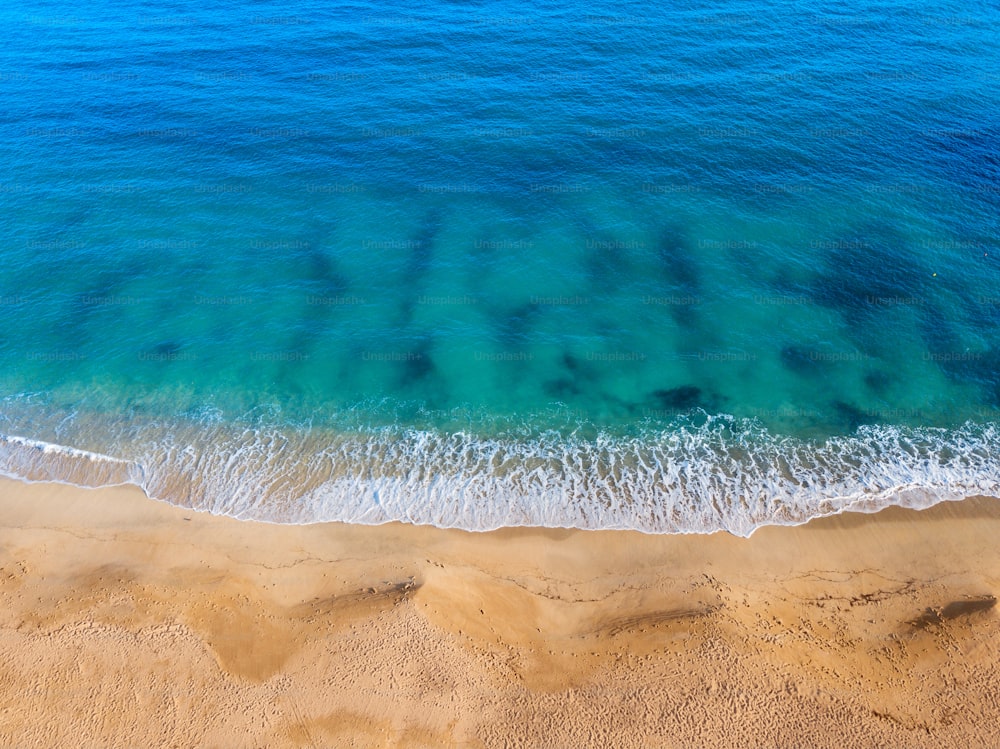 Vista aérea de una idílica playa de arena marina con una ola azul entrante. El concepto de vacaciones en países tropicales y relajación. Antecedentes para viajes y vacaciones