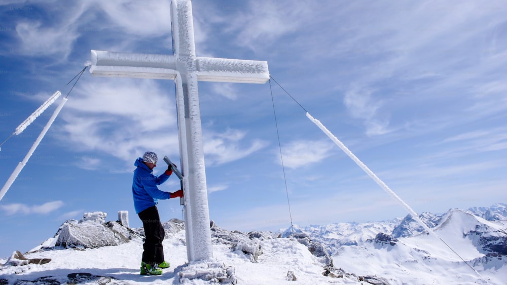 sciatore fuoripista maschio alla croce di vetta di un'alta vetta alpina in una bella giornata invernale in Svizzera