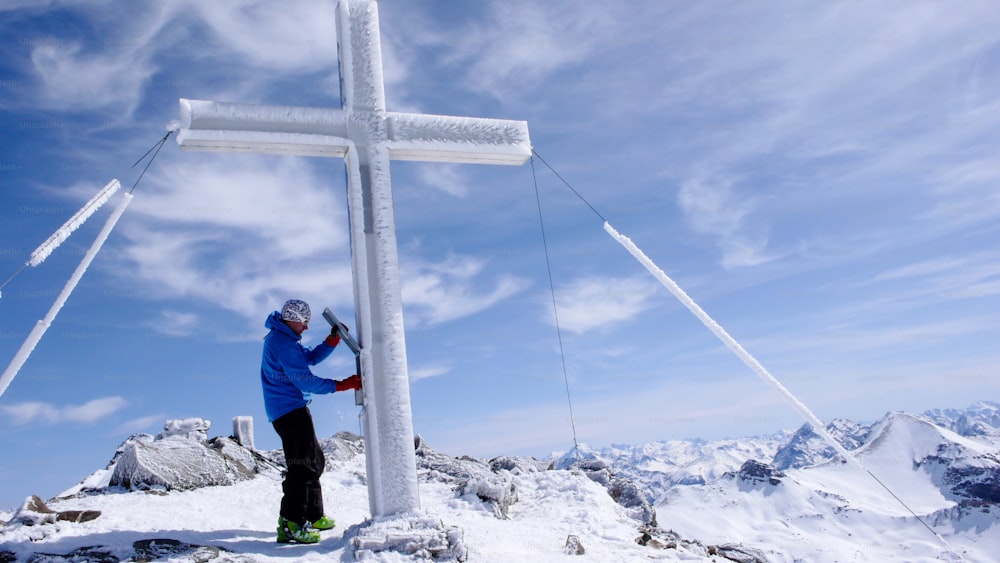 male backcountry skier at the summit cross of a high alpine peak on a beautiful winter day in Switzerland