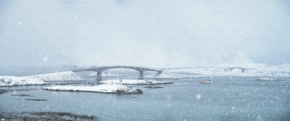 Fredvang bridges in heavy snowfall in winter with fishing ship. Lofoten islands, Norway