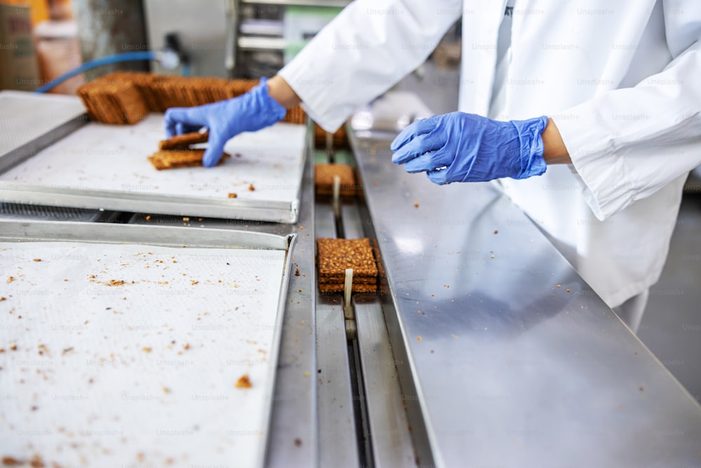 Primo piano dell'operaio che raccoglie i biscotti forma la macchina mentre si trova nella fabbrica alimentare.