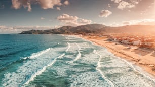 Vue aérienne panoramique spectaculaire de la station balnéaire emblématique de Sarti et de la célèbre plage de sable longue et vide au coucher du soleil avec de hautes vagues. Vacances en Chalcidique, Grèce