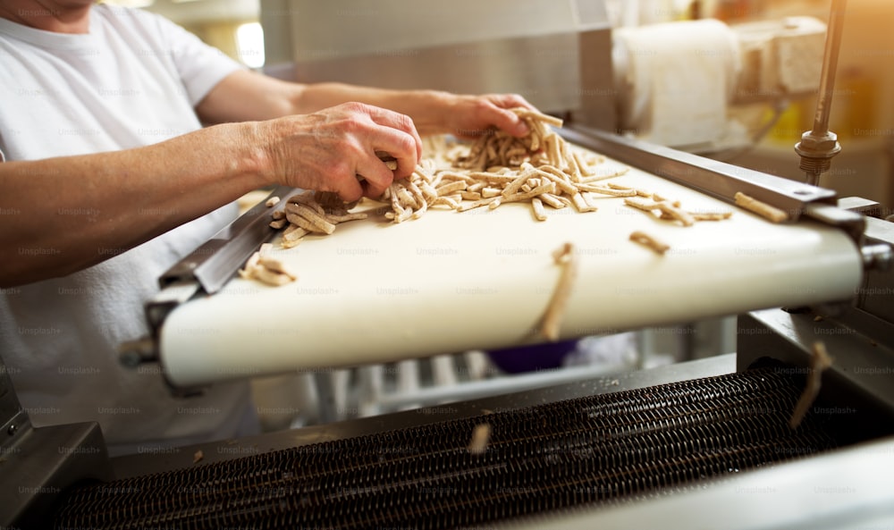 Un travailleur dévoué et prudent et mature répand de la pâte à bâtonnets de sel sur le convoyeur de la ligne de production d’aliments sains pour un traitement ultérieur.