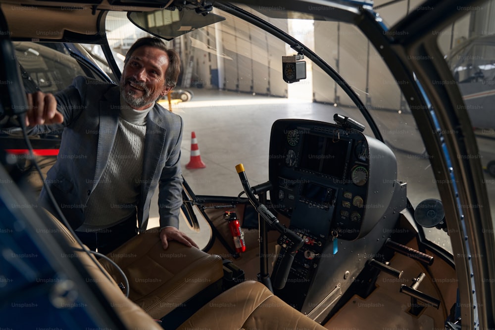 Smiling pleased concentrated mature Caucasian man looking inside open helicopter cockpit