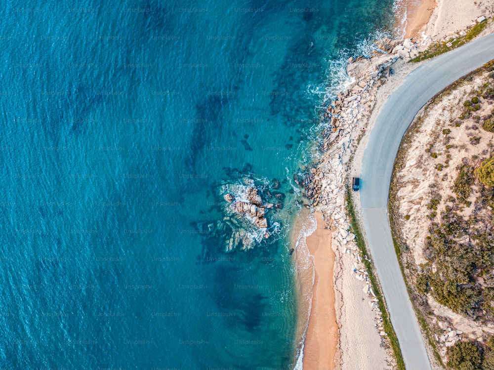Vue aérienne d’une plage de sable idyllique avec une route sinueuse asphaltée et une petite voiture qui roule. Contexte pour les voyages et les vacances