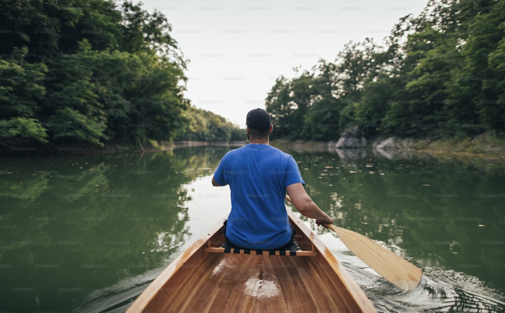 Rear view of man paddling canoe in the lake forest.