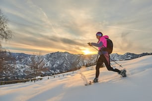 夕日の風景の中でスノーシューで雪の中の下り坂をスポーティな若い女性