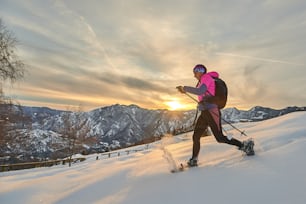 Young sporty woman downhill in the snow with snowshoes in a sunset landscape