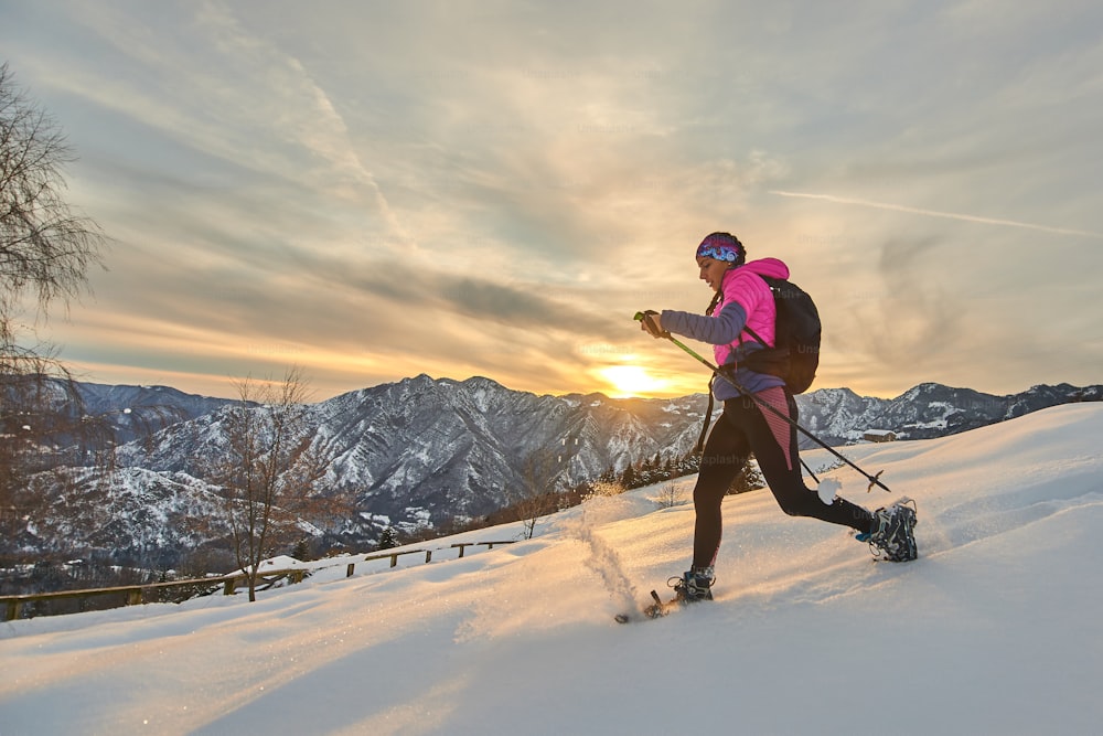 Young sporty woman downhill in the snow with snowshoes in a sunset landscape