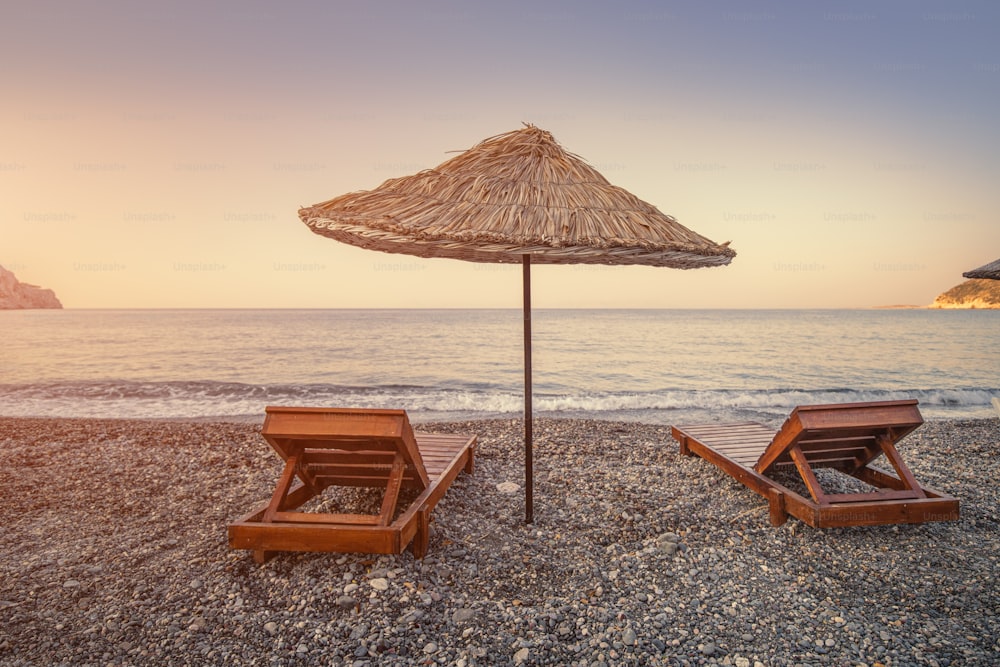 Liegen und Sonnenschirme erwarten Urlauber am Kiesstrand am Strand Ovabuku auf der Halbinsel Datca in der Türkei. Das Foto wurde am frühen Morgen bei Sonnenaufgang aufgenommen