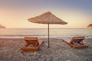 Sunbeds and sun umbrellas await vacationers on the shingle beach at Ovabuku beach on the Datca Peninsula in Turkey. The photo was taken in the early morning at sunrise