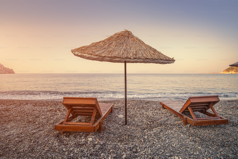 Sunbeds and sun umbrellas await vacationers on the shingle beach at Ovabuku beach on the Datca Peninsula in Turkey. The photo was taken in the early morning at sunrise