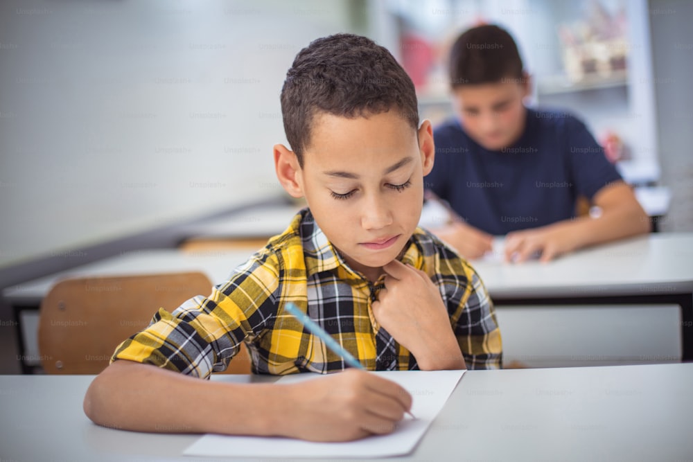 Estudiantes adolescentes sentados en el aula y escribiendo un examen. La atención se centra en el fondo.
