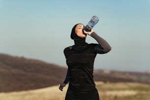 Female athlete drinking water while jogging in the morning in nature.