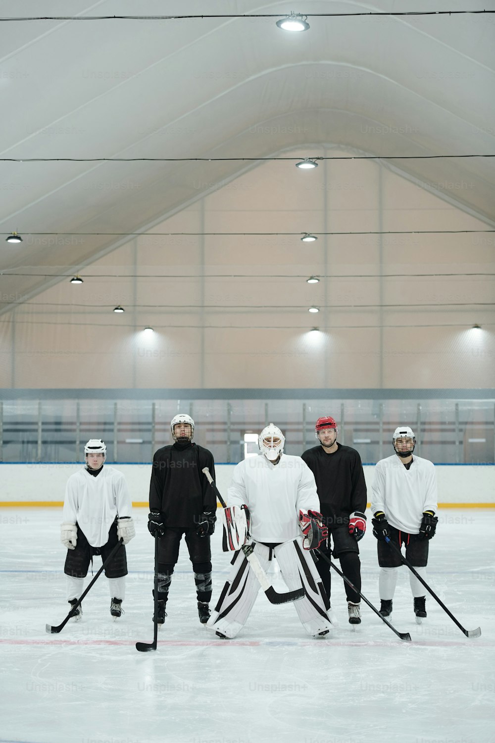 Gruppe von Hockeyspielern und ihrem Trainer in Sportuniform, Handschuhen, Schlittschuhen und Schutzhelmen, die auf der Eisbahn stehen und auf das Spiel warten