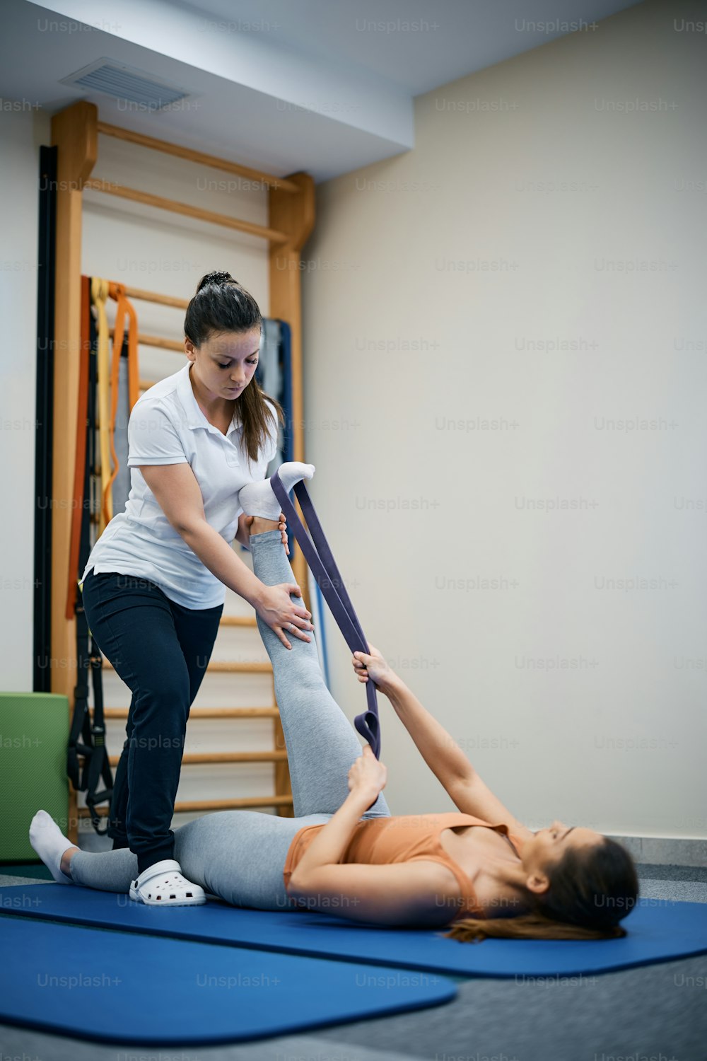 リハビリテーションセンターで理学療法士の助けを借りて脚を鍛えながらパワーバンドを使用する運動女性。