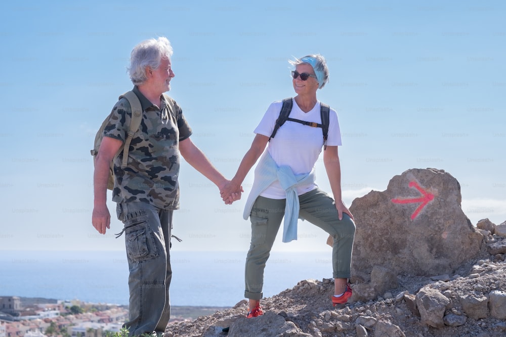 Happy active senior couple in outdoor excursion hiking in mountain with backpack  enjoying healthy lifestyle.  Horizon over water on background