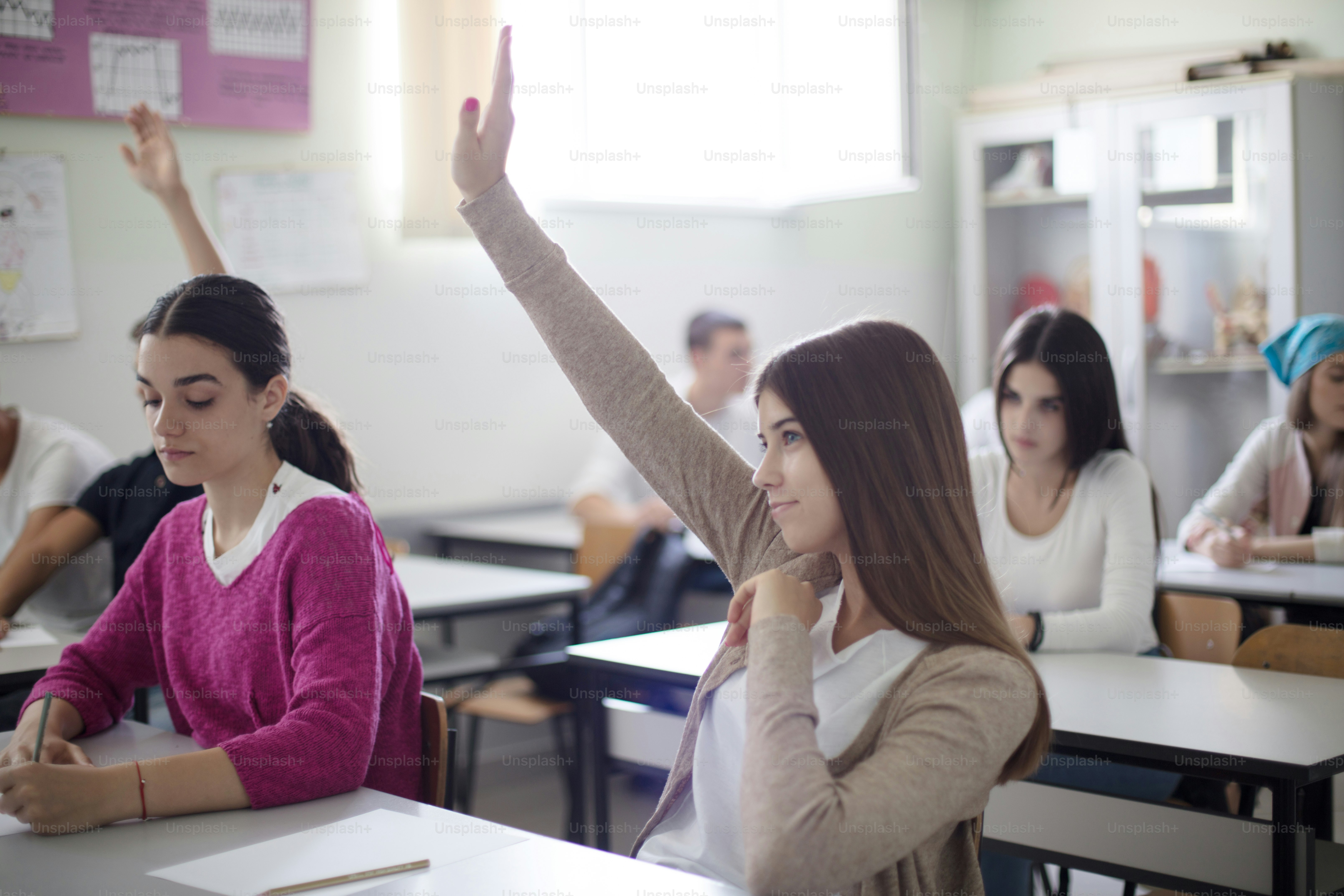 Es muy inteligente.  Los estudiantes adolescentes sentados en el aula levantan la mano. Retrato de una alumna.