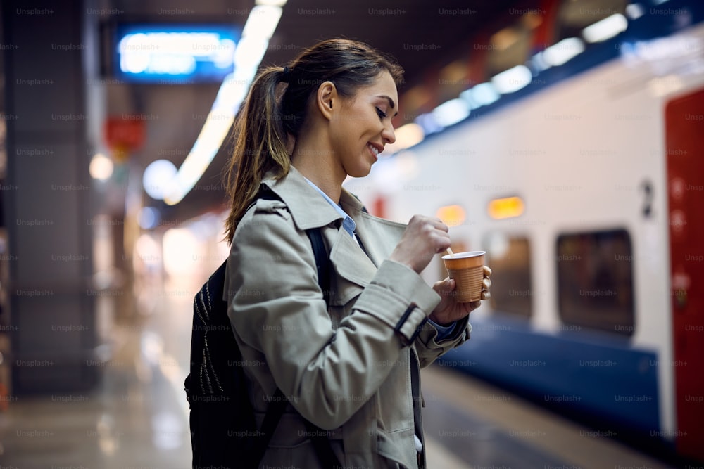 Young happy woman drinking takeaway coffee while waiting for train in a subway.