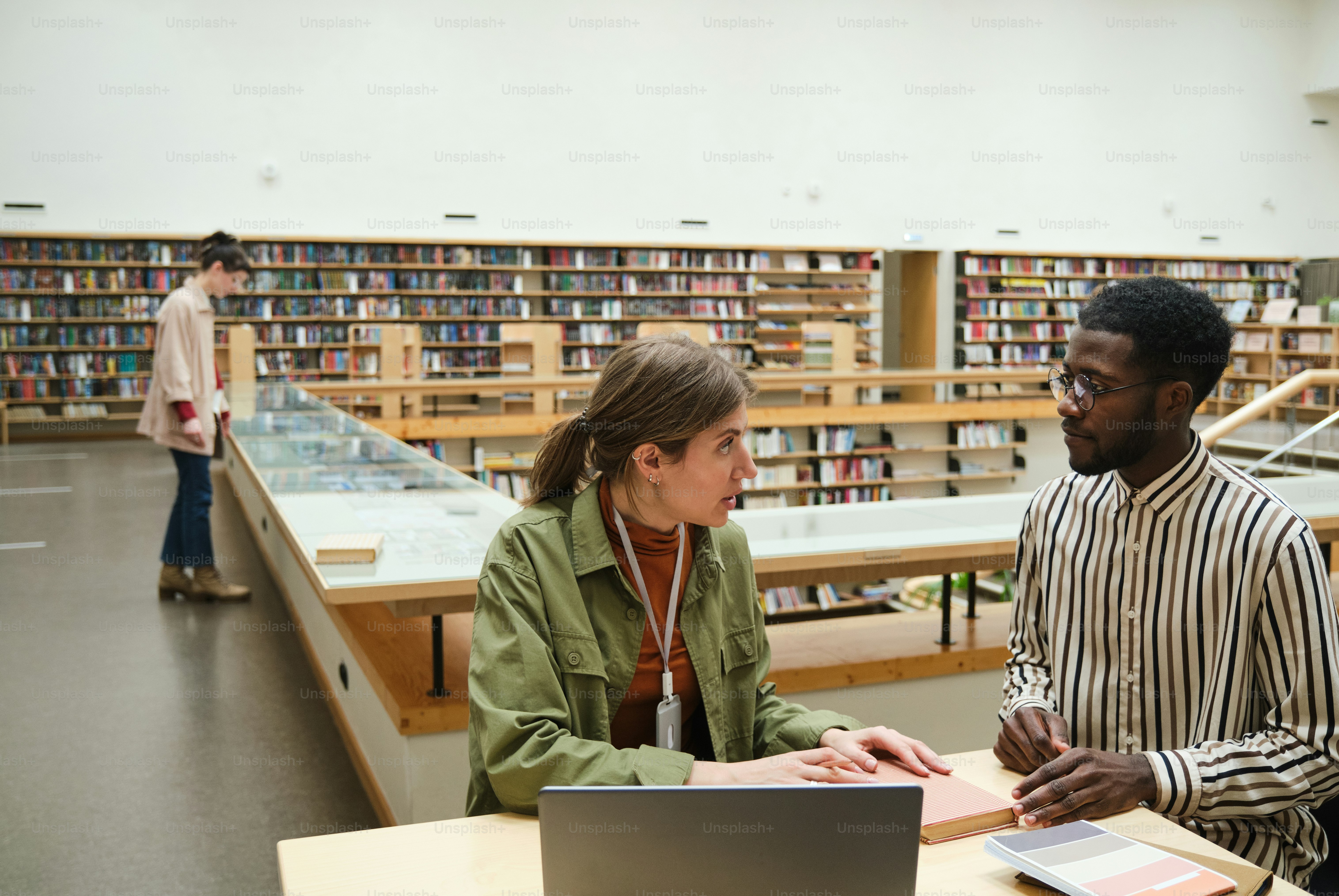 Jóvenes trabajando juntos en la mesa y discutiendo la lectura de los libros de la biblioteca
