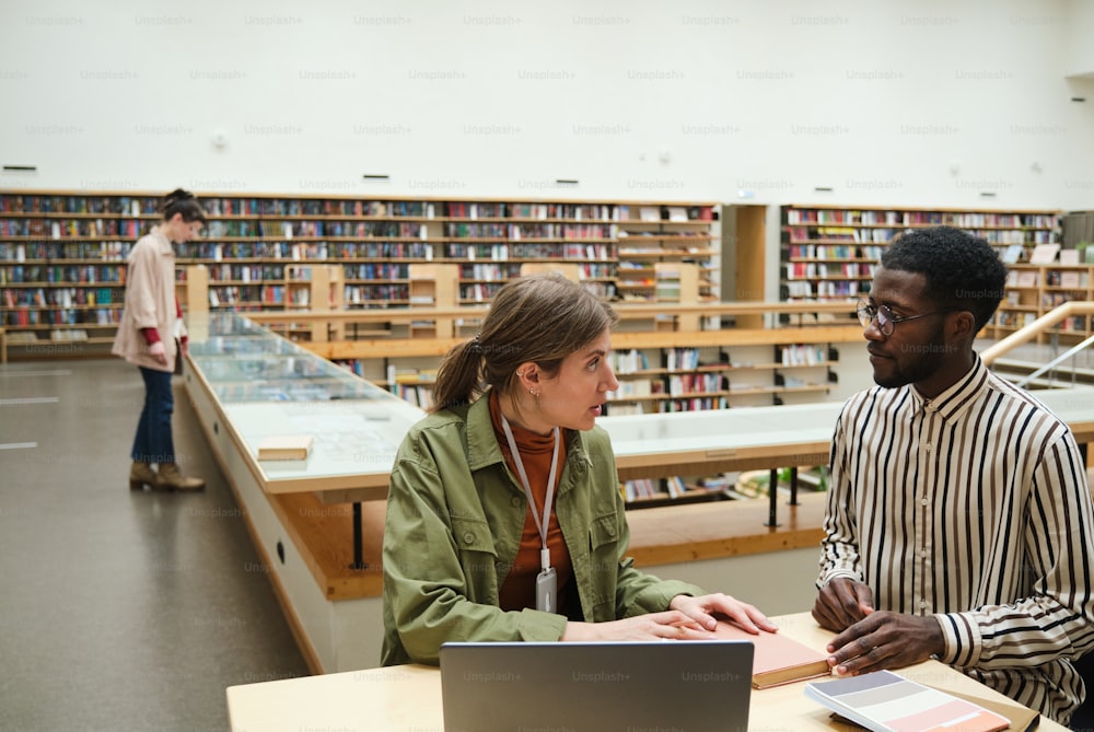 Young people working at the table together and discussing reading of the books in the library